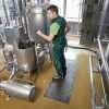 A man in a green overalls using a blue hose to fill a stainless steel tank with water white standing on a Morland Service Anti Bacterial Industrial rubber Doormat