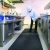 A Chief at a stove in a commercial kitchen turning a dial stood on a Morland Service Anti bacterial rubber industrial doormat