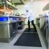 A Chief at a stove in a commercial kitchen with large frying pan stood on a Morland Service Anti bacterial rubber industrial doormat
