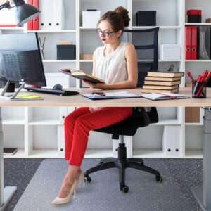 A young girl sits at a computer table and holds an open book in her hands.